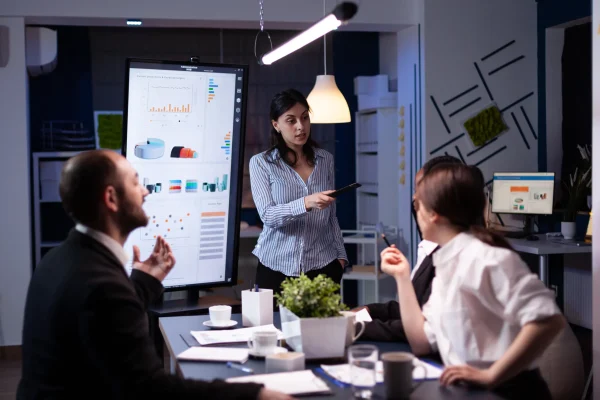 empresaria-adicta-al-trabajo-que-senala-la-estrategia-financiera-usando-el-monitor-trabajando-horas-extras-en-la-sala-de-la-oficina-de-reuniones-de-la-empresa